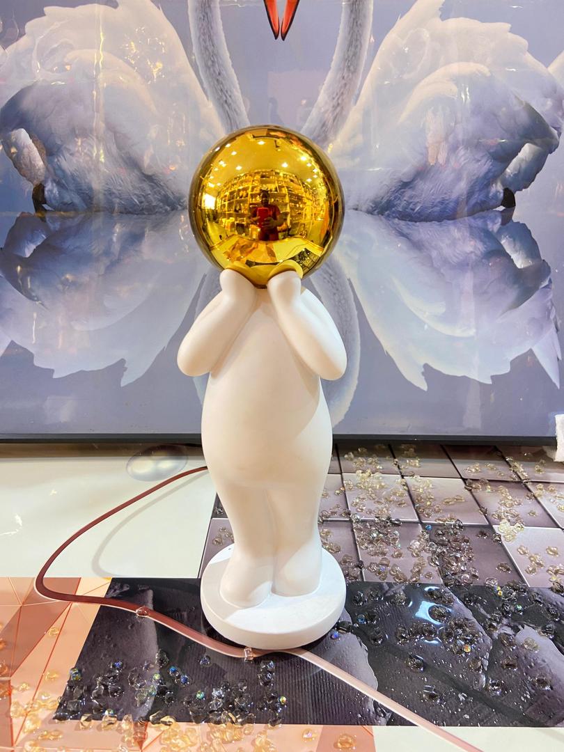 White rounded figure holding gold mirror ball